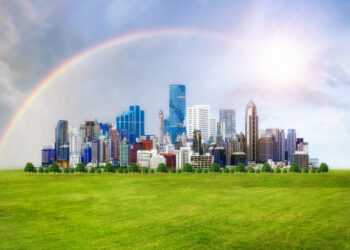 Modern city view with beautiful buildings on green grass, rainbow on sky and the sun, Green city concept.
