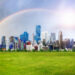 Modern city view with beautiful buildings on green grass, rainbow on sky and the sun, Green city concept.