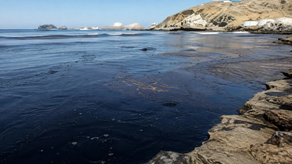 Vista de una playa de Ancón afectada por hidrocarburos, con presencia de contaminación en la costa y aves marinas en el entorno.